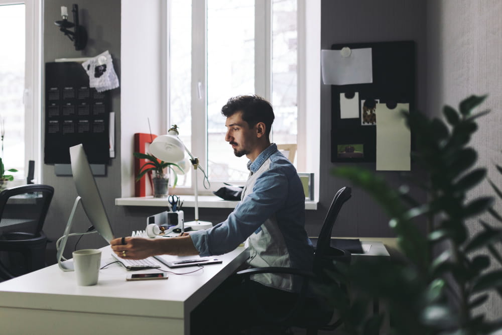 a man working in office on laptop in blue and grey shirt
