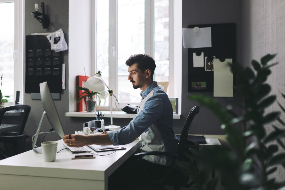 a man working in office on laptop in blue and grey shirt